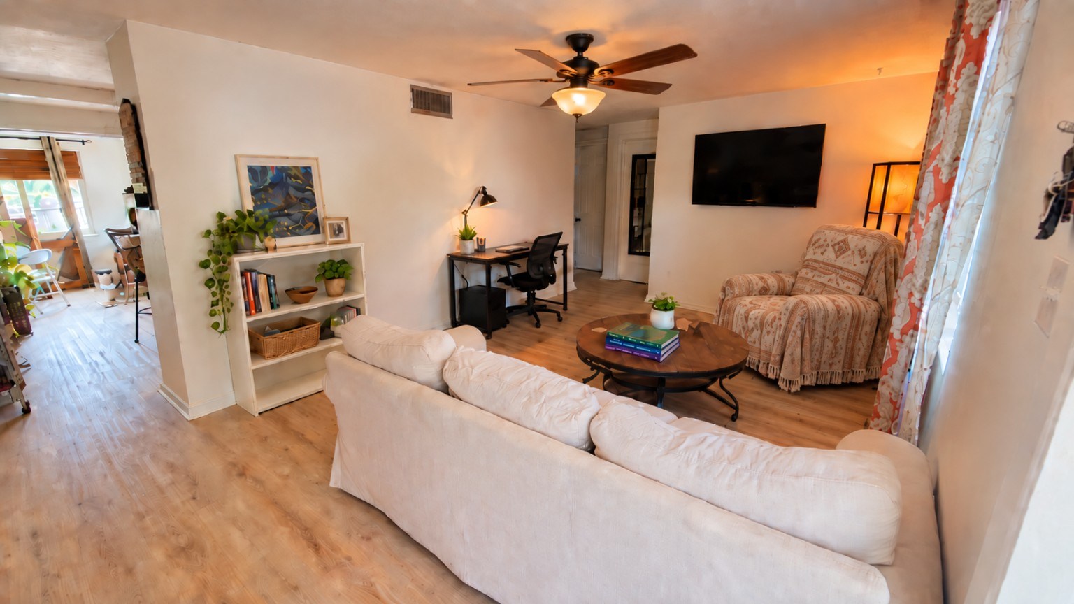 Furnished living room with sofa, covered recliner, TV, bookshelf, and desk